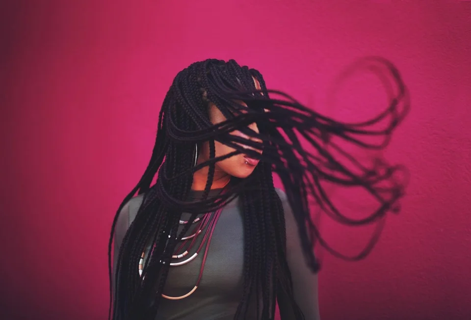 Expressive long braids in motion against a rich pink background